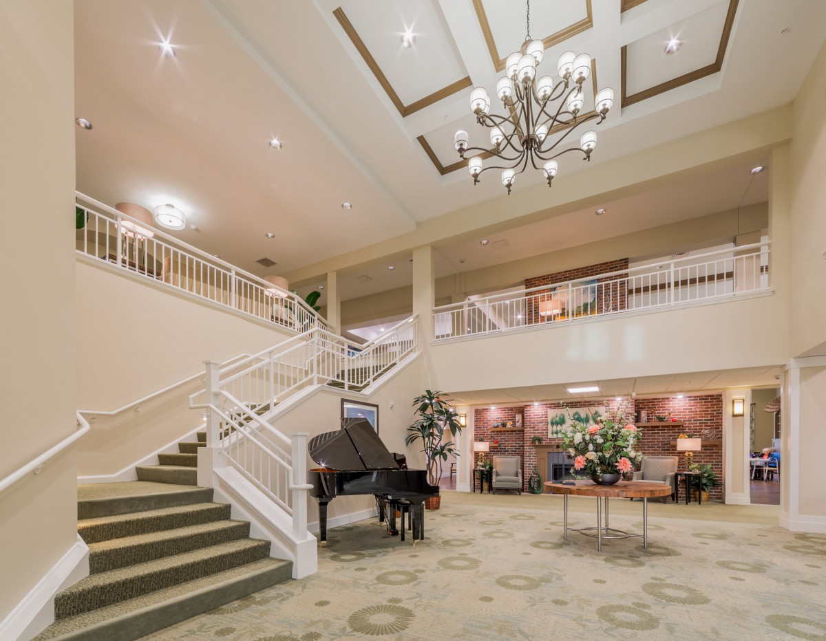 An elegant hotel lobby featuring a grand chandelier, a piano, and a wide staircase.