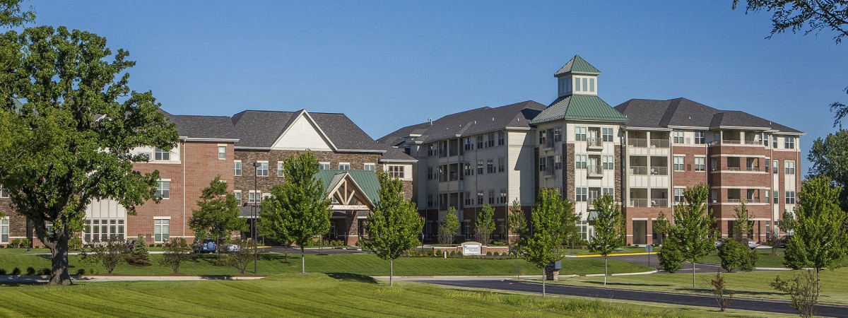 A scenic view of residential buildings surrounded by trees and a well-maintained lawn on a sunny day.
