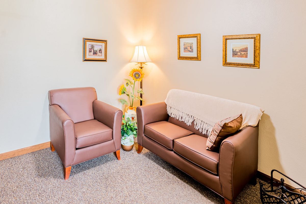A cozy living room with a sofa, armchair, decorative lamp, and framed pictures.