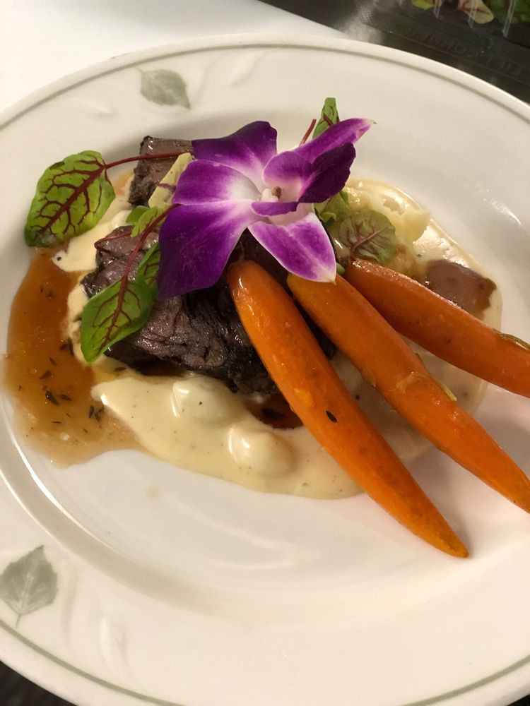 A gourmet dish featuring beef, carrots, and mashed potatoes, elegantly garnished with an edible flower.