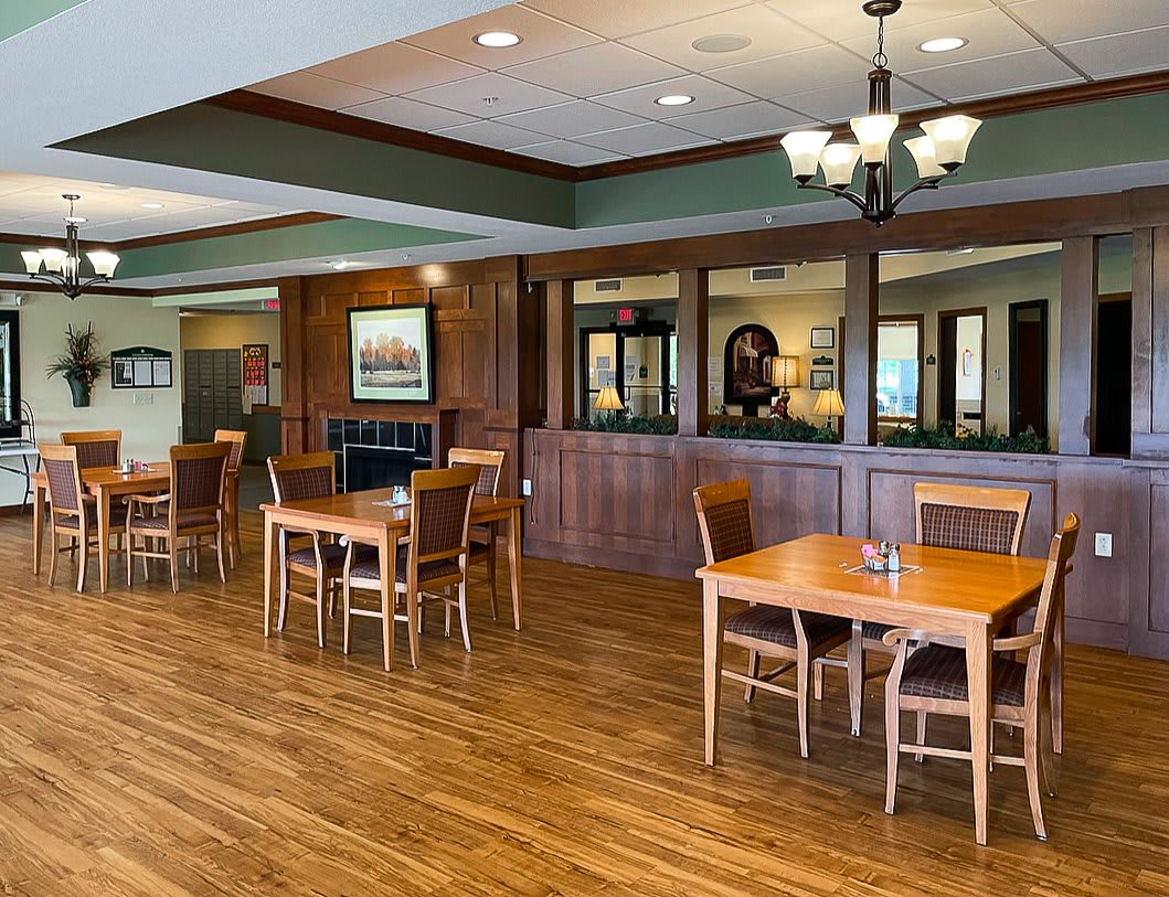 An empty dining area with wooden tables and chairs, featuring a chandelier and laminate flooring.