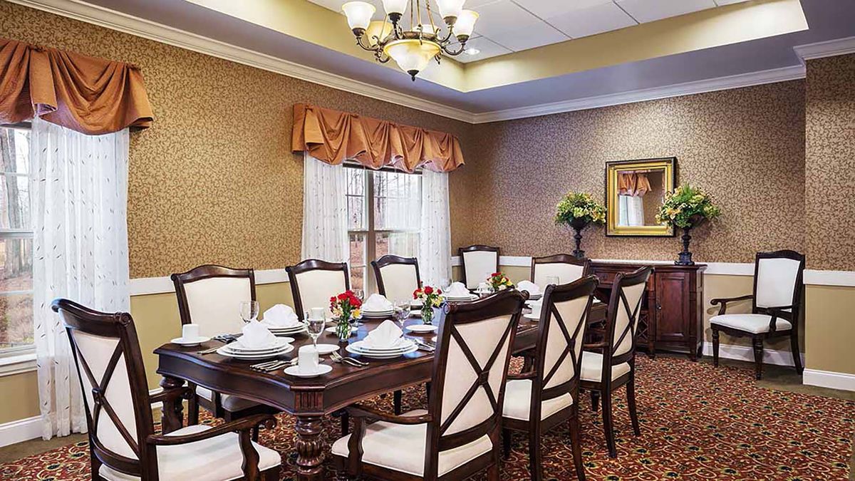 An elegantly set dining room with a large table, upholstered chairs, and a chandelier.