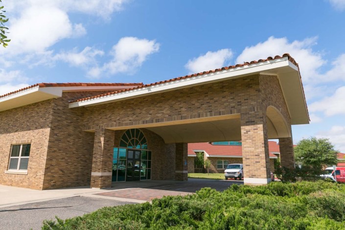 A view of a building entrance with a covered drive-through area against a backdrop of blue sky and clouds.