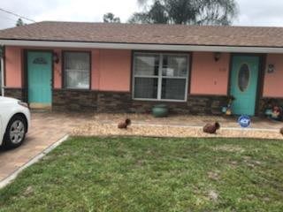 A quaint house with orange walls and turquoise doors, featuring a yard with two chickens.