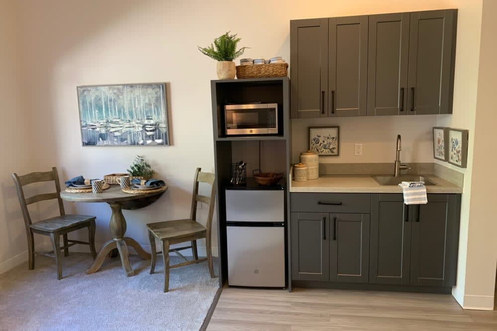 A small kitchenette with a microwave, mini refrigerator, and cabinetry alongside a table and chairs.