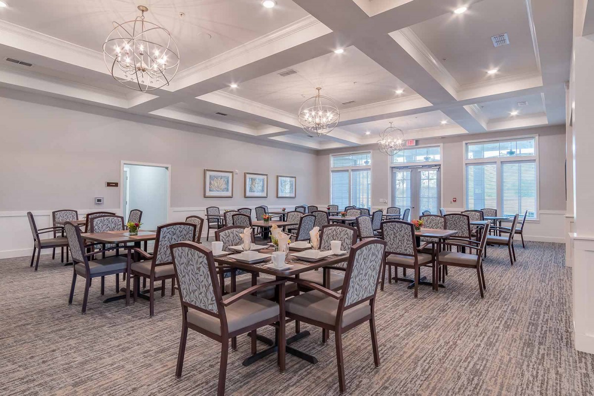 A spacious and elegantly furnished dining room with neatly arranged tables and chairs under chandeliers.