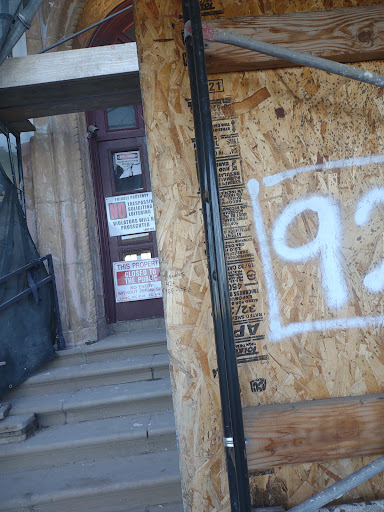 A boarded-up entrance to an abandoned building, featuring graffiti and a faded number on the wooden panel.