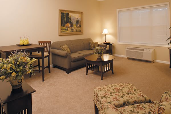 A cozy living room with a sofa, tables, and a lamp, decorated with a painting on the wall.