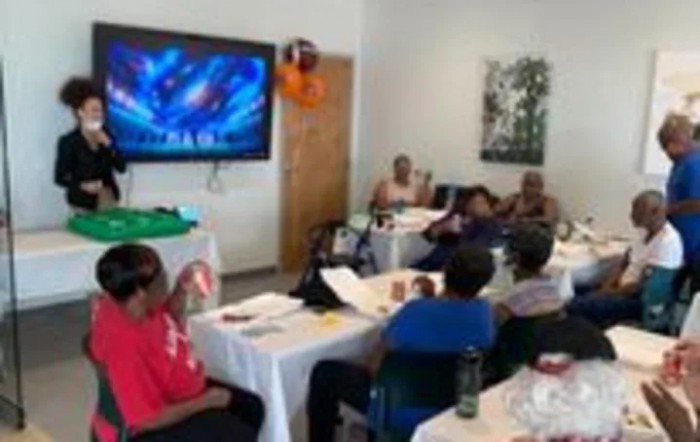 A group of people attending a meeting or presentation in an indoor setting, with a television screen displaying content.
