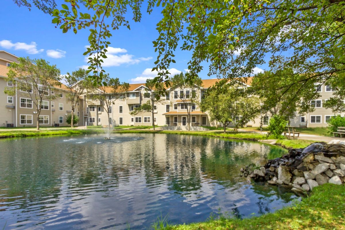 A serene residential building surrounded by a picturesque pond and lush greenery.