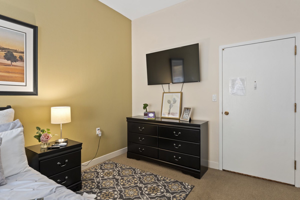 A cozy bedroom featuring a dresser with a mounted television, a stylish lamp, and decorative elements.