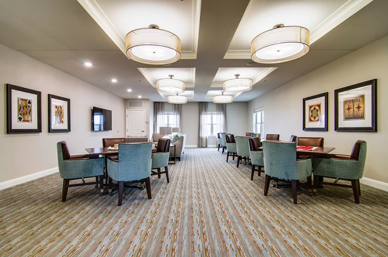 A modern dining room with elegantly arranged tables and chairs, featuring soft lighting and a carpeted floor.