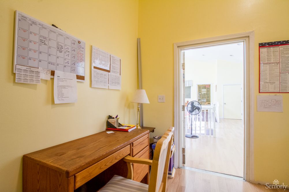 A cozy home office with a wooden desk and chair against a yellow wall, featuring documents pinned on the wall.