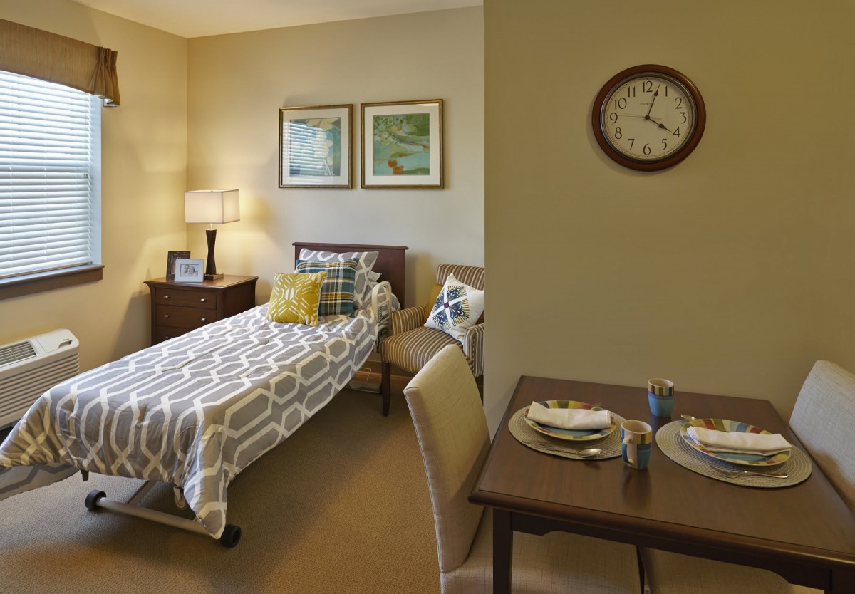A cozy bedroom with a single bed, nightstand, and a small dining table set.