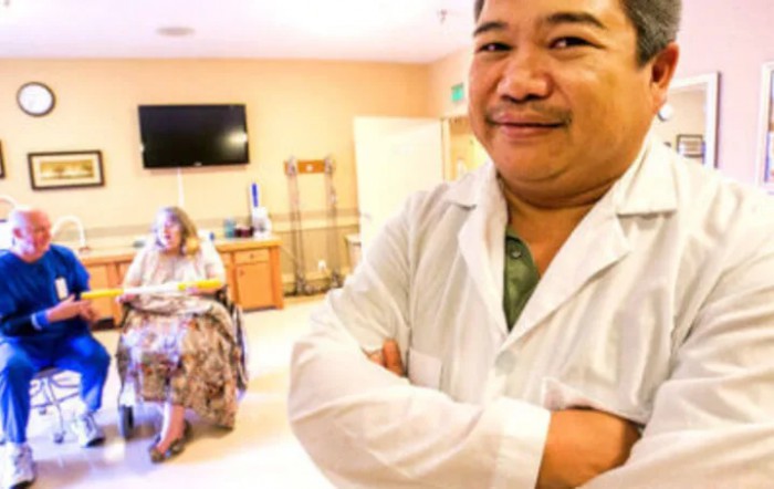 A doctor standing confidently in a hospital room with a patient in the background.
