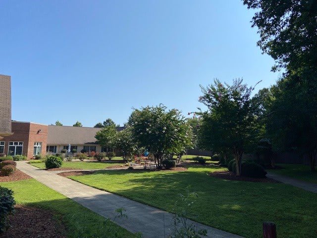 A sunny day with a view of a landscaped garden, trees, and a building in the background.