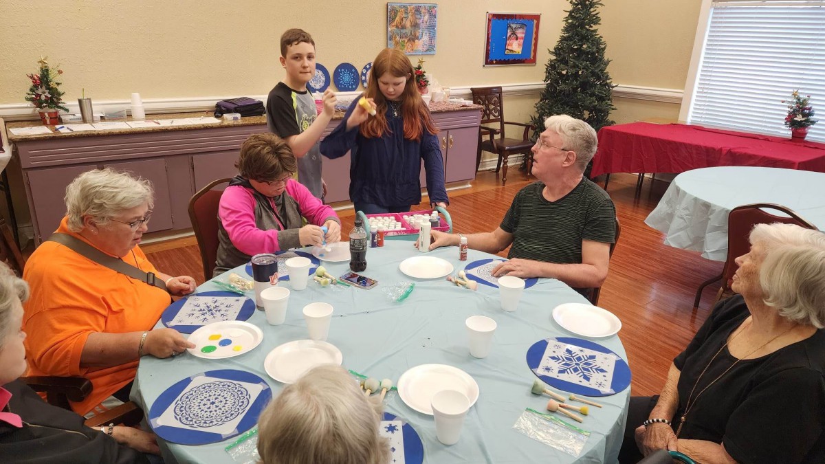 A group of adults and children engaged in an art activity around a table.