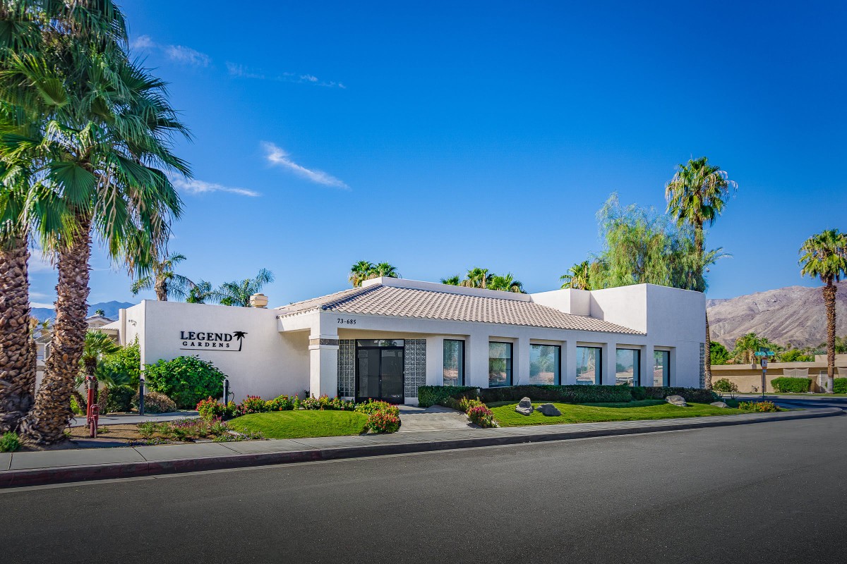A modern office building surrounded by palm trees under a clear blue sky.