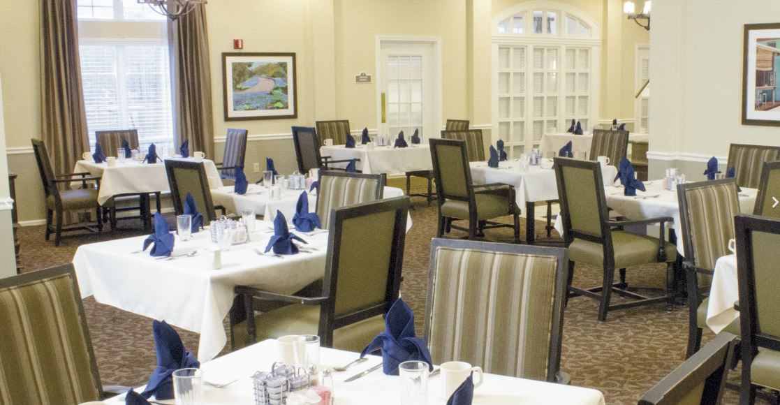 A well-appointed dining room with neatly arranged tables and chairs, featuring elegant table settings with folded napkins.