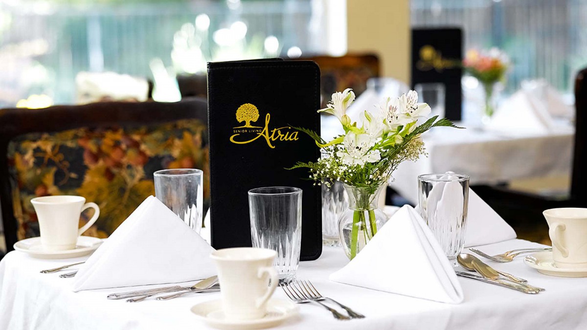 An elegantly set restaurant table with a menu and flower arrangement.
