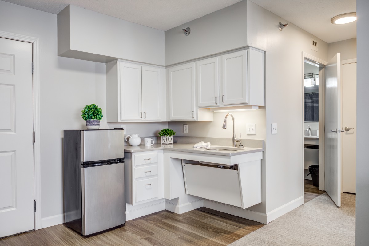 A modern, minimalist kitchen featuring white cabinets and a small stainless steel fridge.