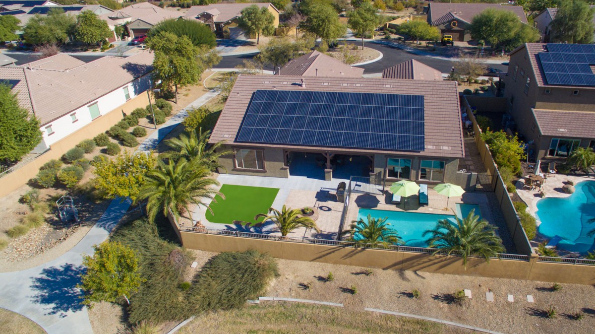 Aerial view of a residential house with solar panels, a pool, and landscaped backyard.