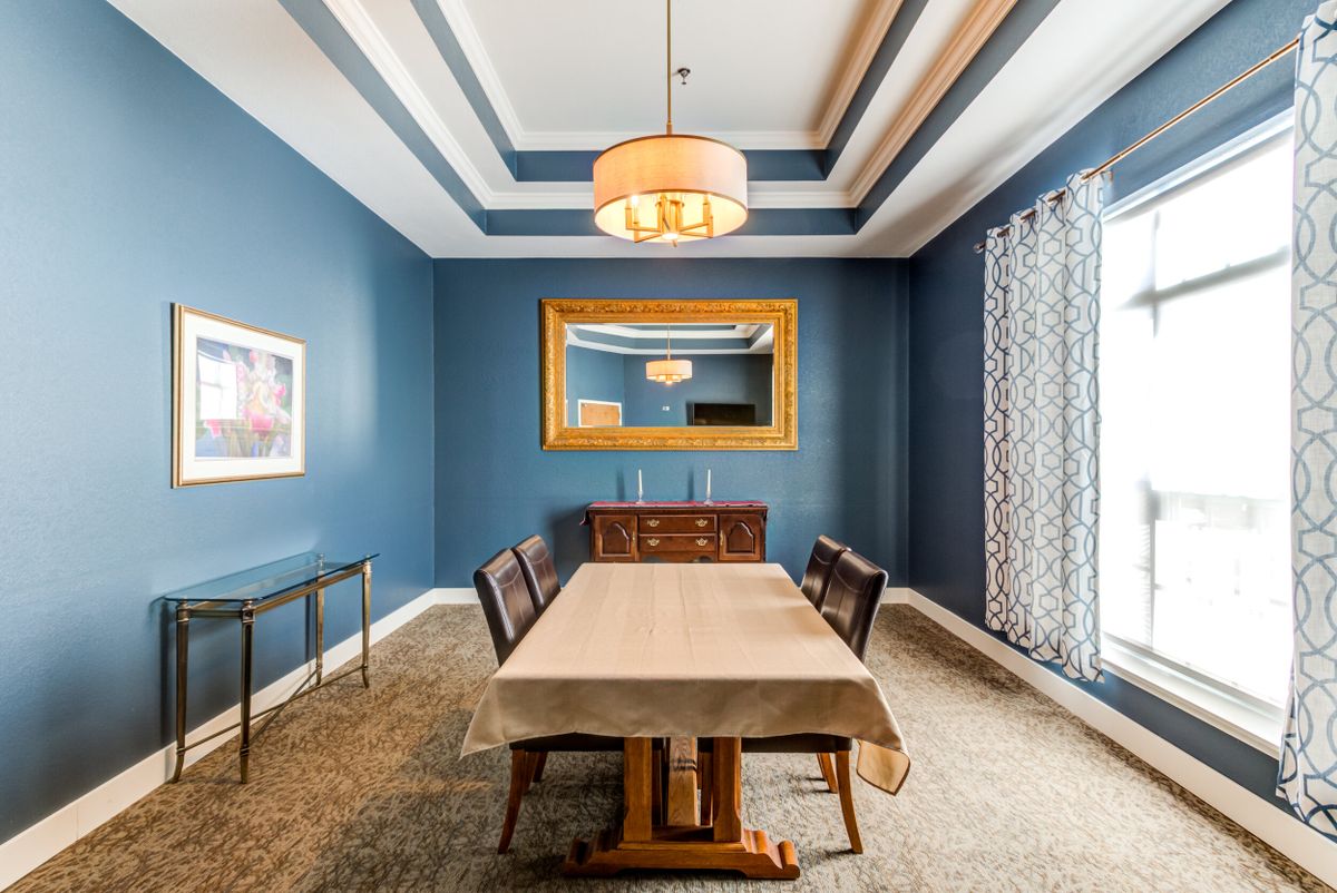 A stylish dining room with blue walls, featuring a large table, elegant chairs, and a central chandelier.