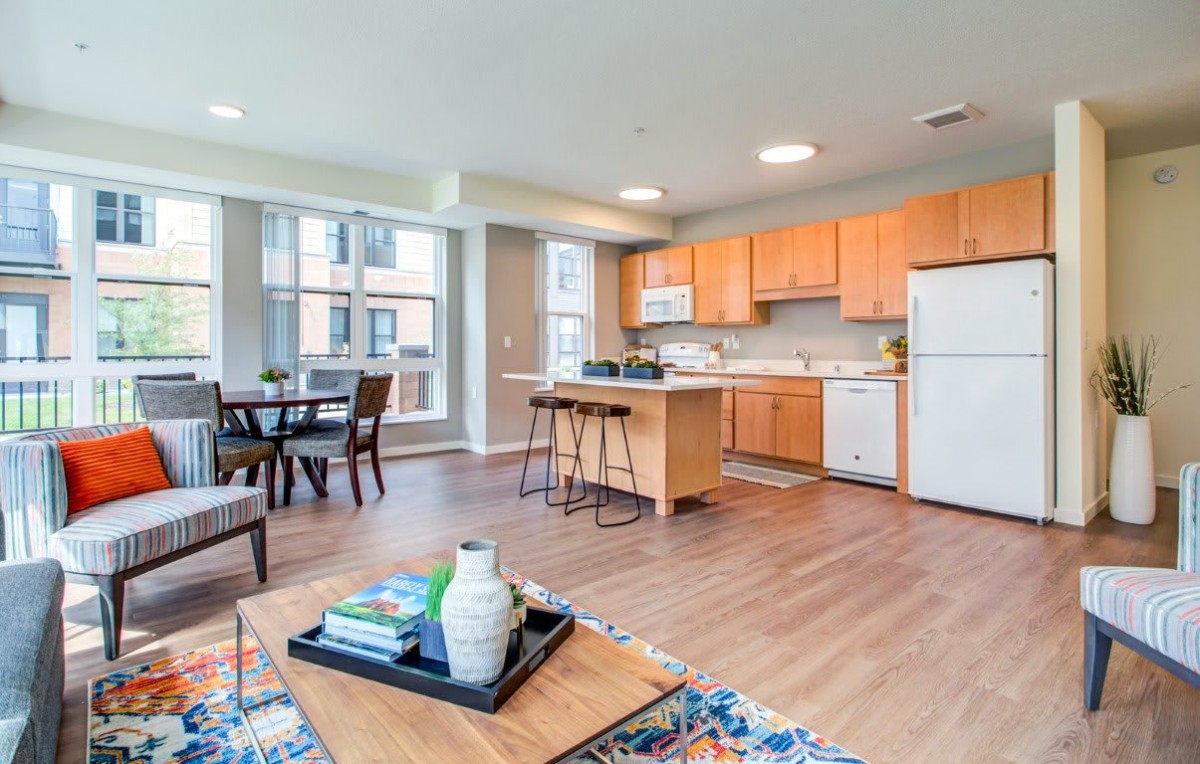A modern apartment showcasing an open floor plan with a kitchen and living area, featuring stylish furniture and large windows for natural light.
