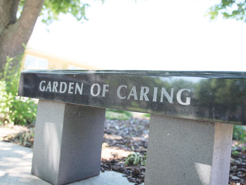A memorial bench engraved with 'Garden of Caring' located outdoors in a garden setting.