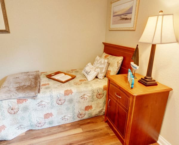 A cozy bedroom corner featuring a single bed with decorative pillows and a nightstand with a lamp.