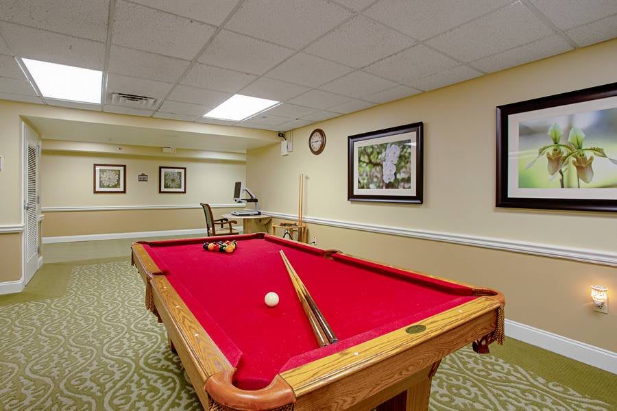 A recreation room featuring a red-felt pool table surrounded by framed art on the walls and carpeted floors.