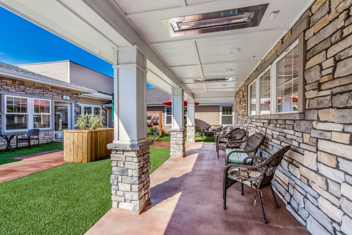 A cozy patio with stone columns and comfortable chairs overlooks a well-kept lawn.