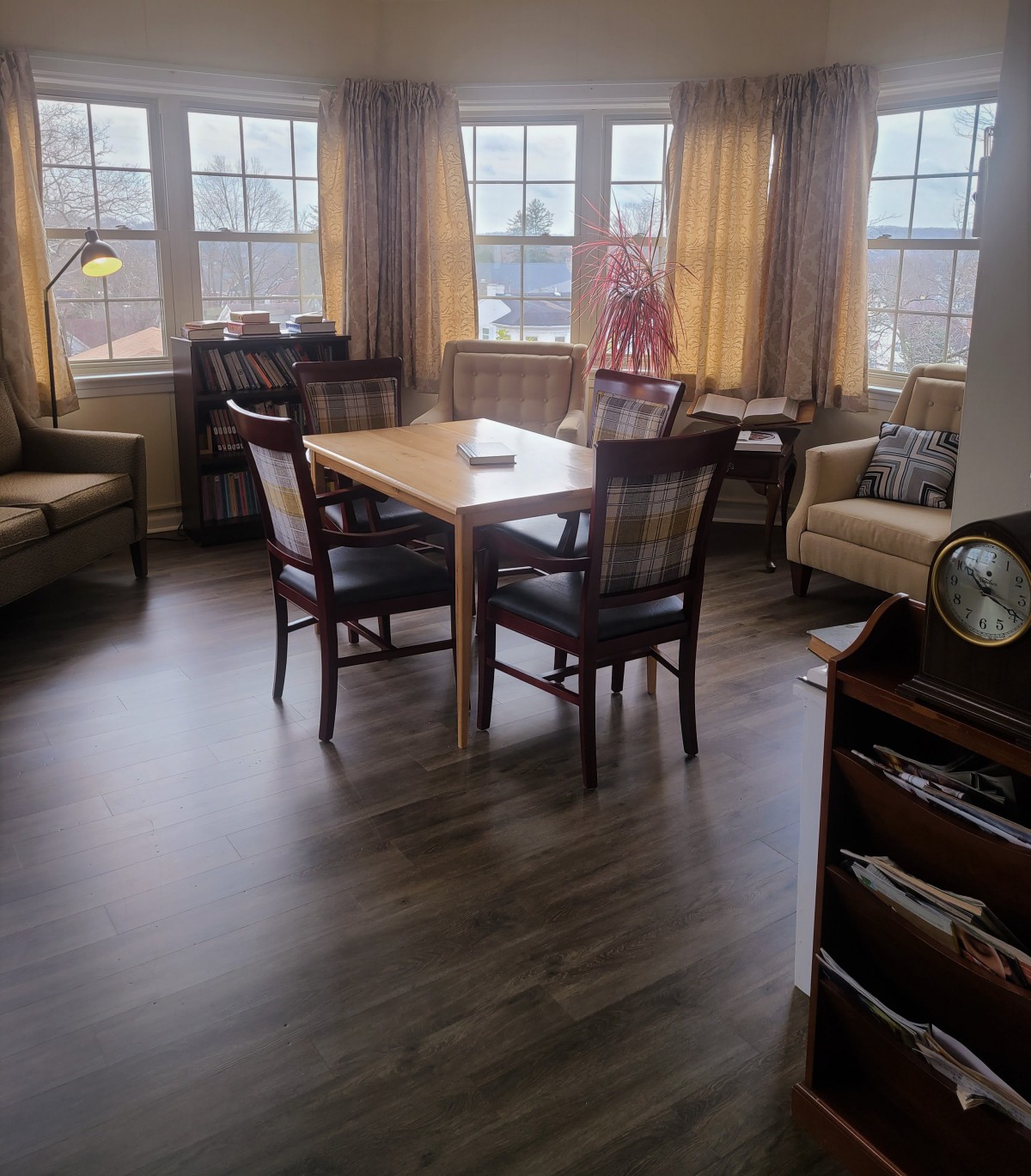 A cozy living room with a dining table set surrounded by armchairs and large windows.