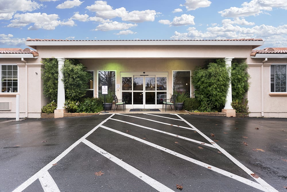 Front entrance of a building with a parking lot and cloudy sky in the background.