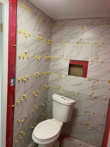 A partially renovated bathroom featuring a toilet and tiled walls.