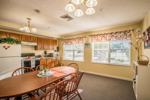 A cozy kitchen and dining area featuring wooden cabinetry, a dining table with chairs, and large windows with floral curtains.