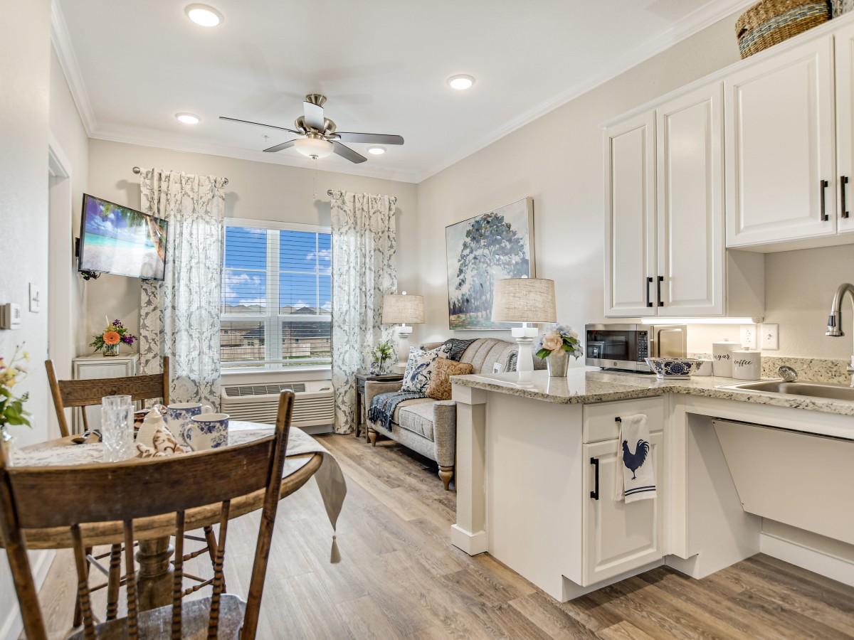A modern open-concept living space combining a dining area, kitchen, and living room with wood flooring and a ceiling fan.