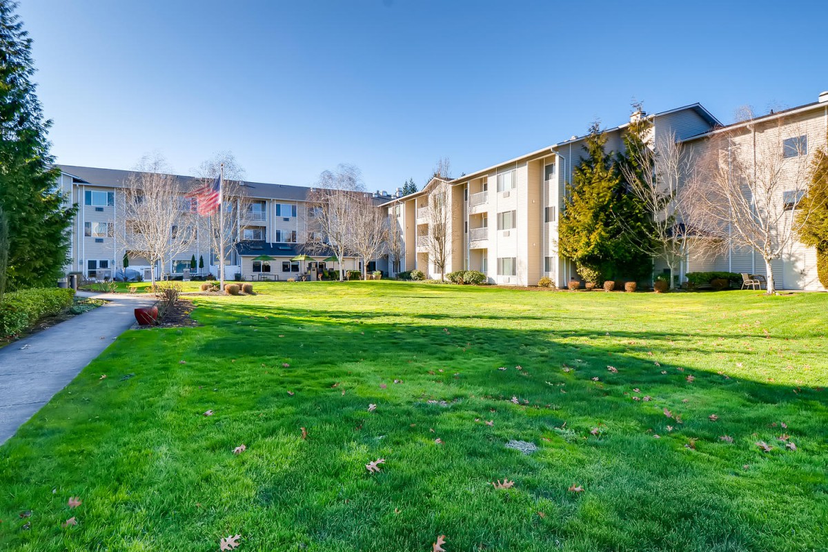 A residential apartment building with a well-maintained lawn and trees under a clear blue sky.