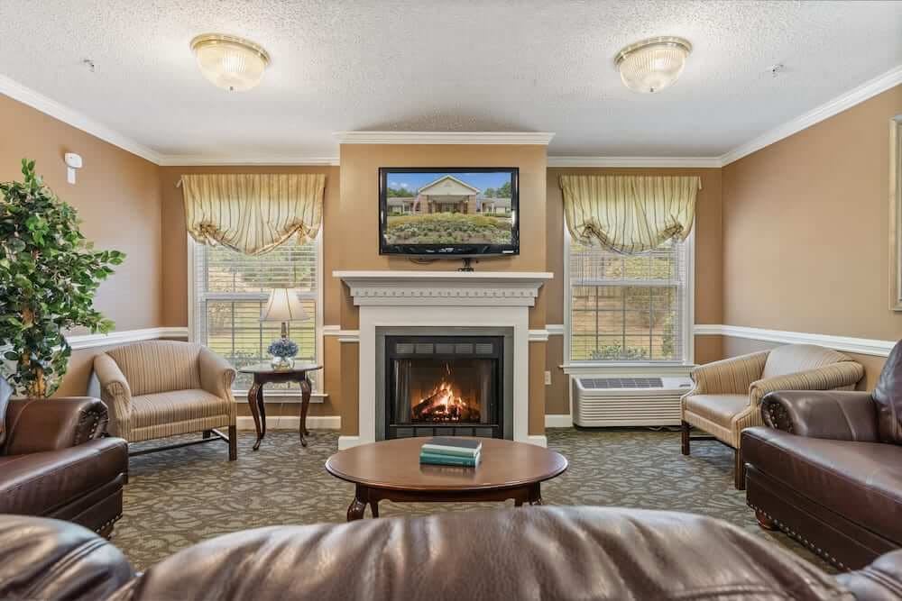 A cozy living room featuring a fireplace and a television mounted above it, surrounded by comfortable seating and large windows.