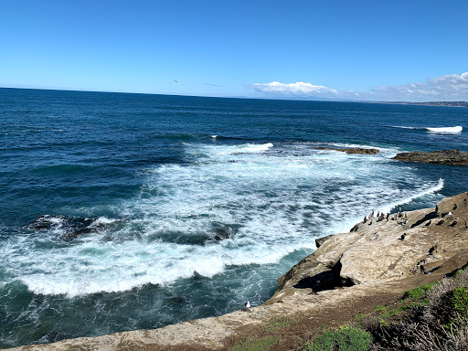 A beautiful coastal view with waves crashing against the rocks under a clear blue sky.