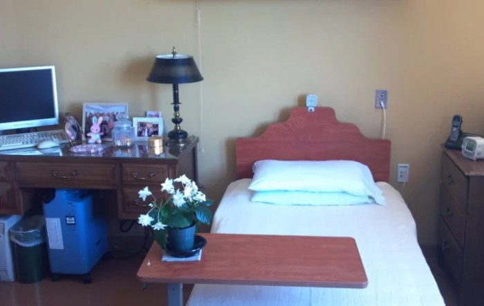 A hospital room with a single bed, side table, and personal items displayed.