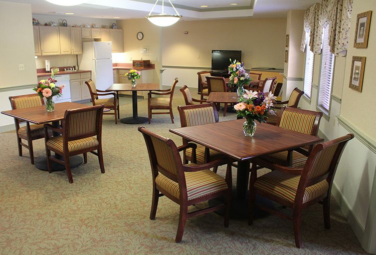 A well-lit dining area with tables and chairs, featuring floral centerpieces and a television.