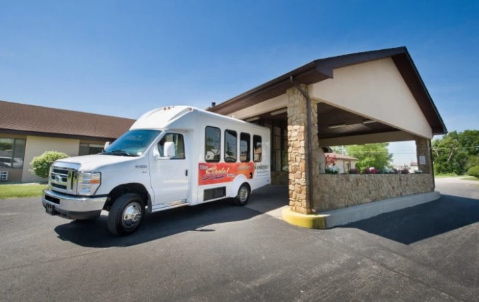 A shuttle van parked in front of a building driveway on a sunny day.