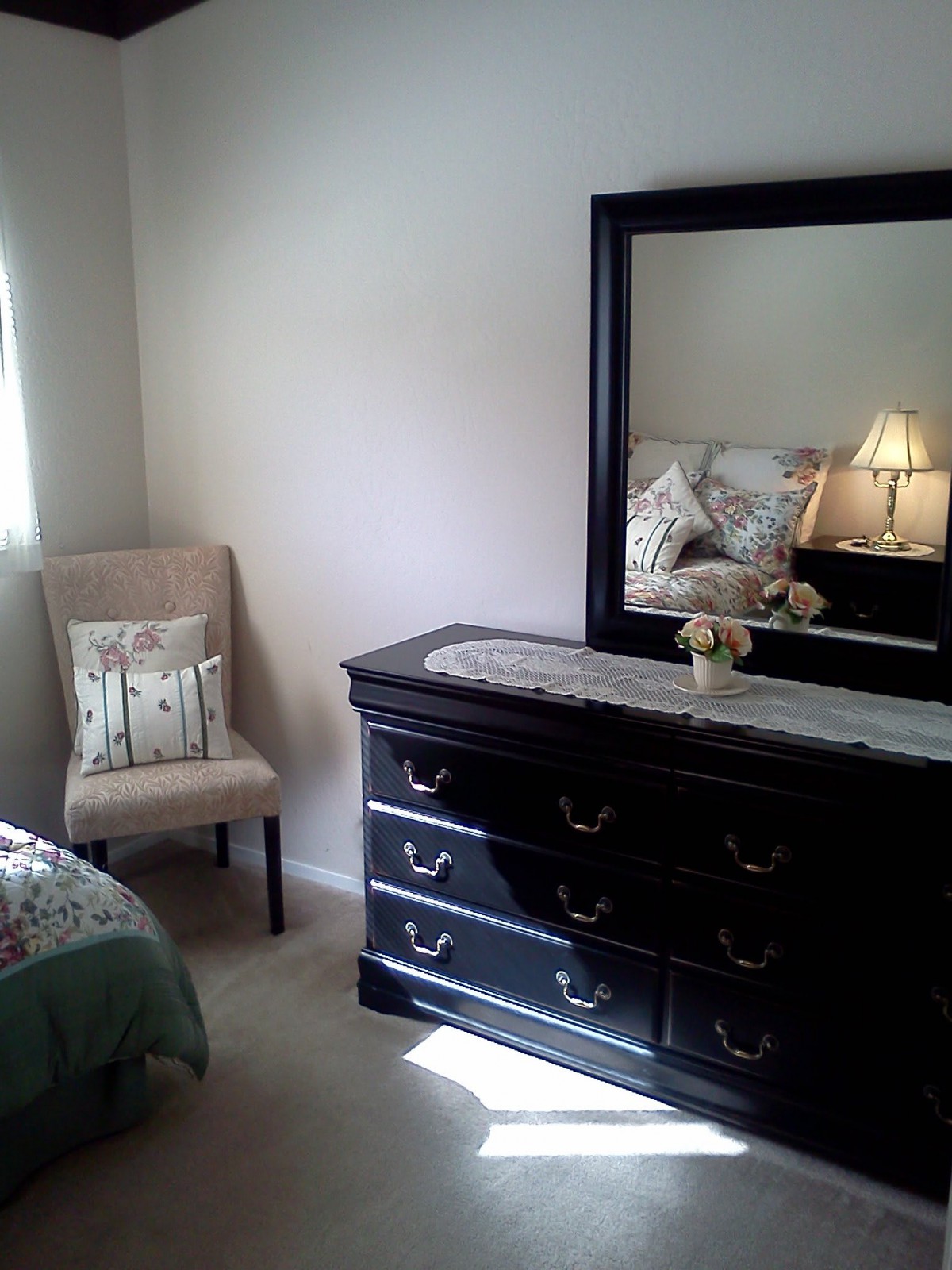 A cozy bedroom with a dresser and mirror, featuring a chair and a lamp for added comfort.