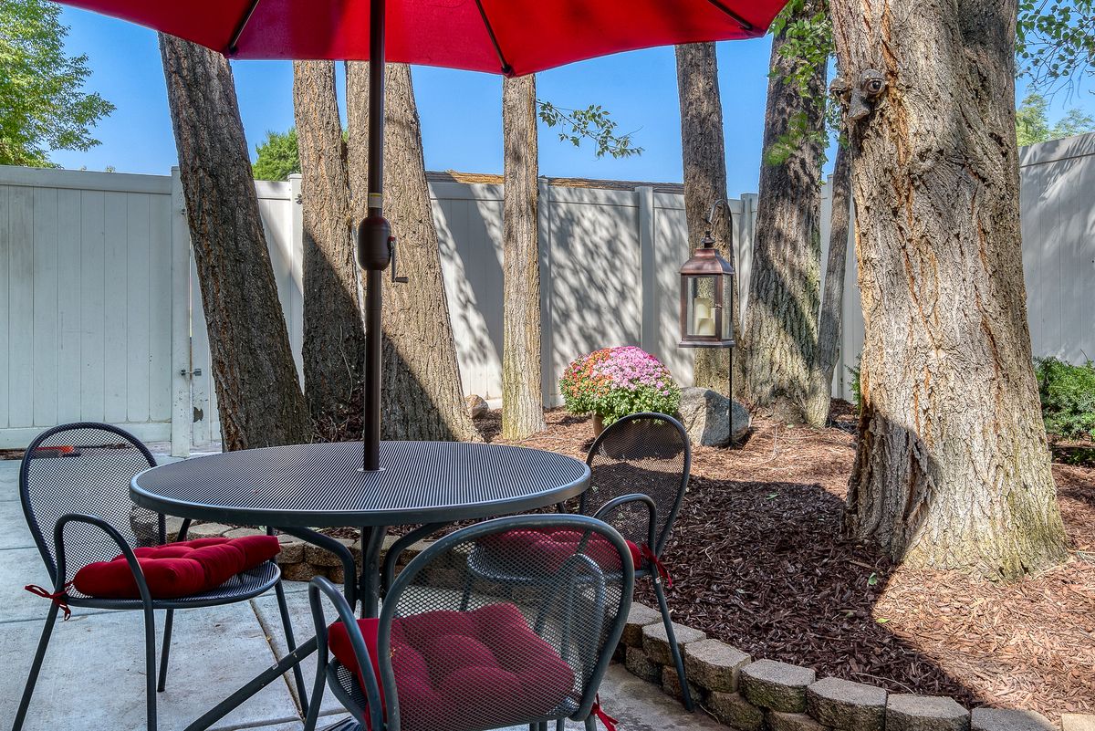 A cozy outdoor patio with a red umbrella, surrounded by trees and a garden.