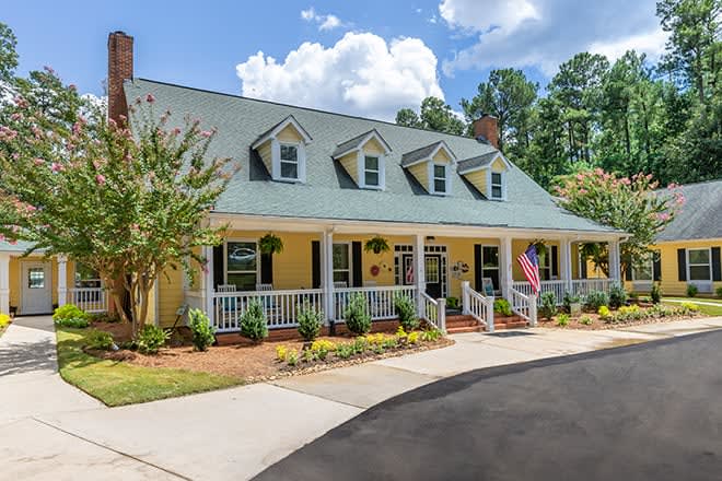 A charming yellow house with a spacious front porch and landscaped yard.