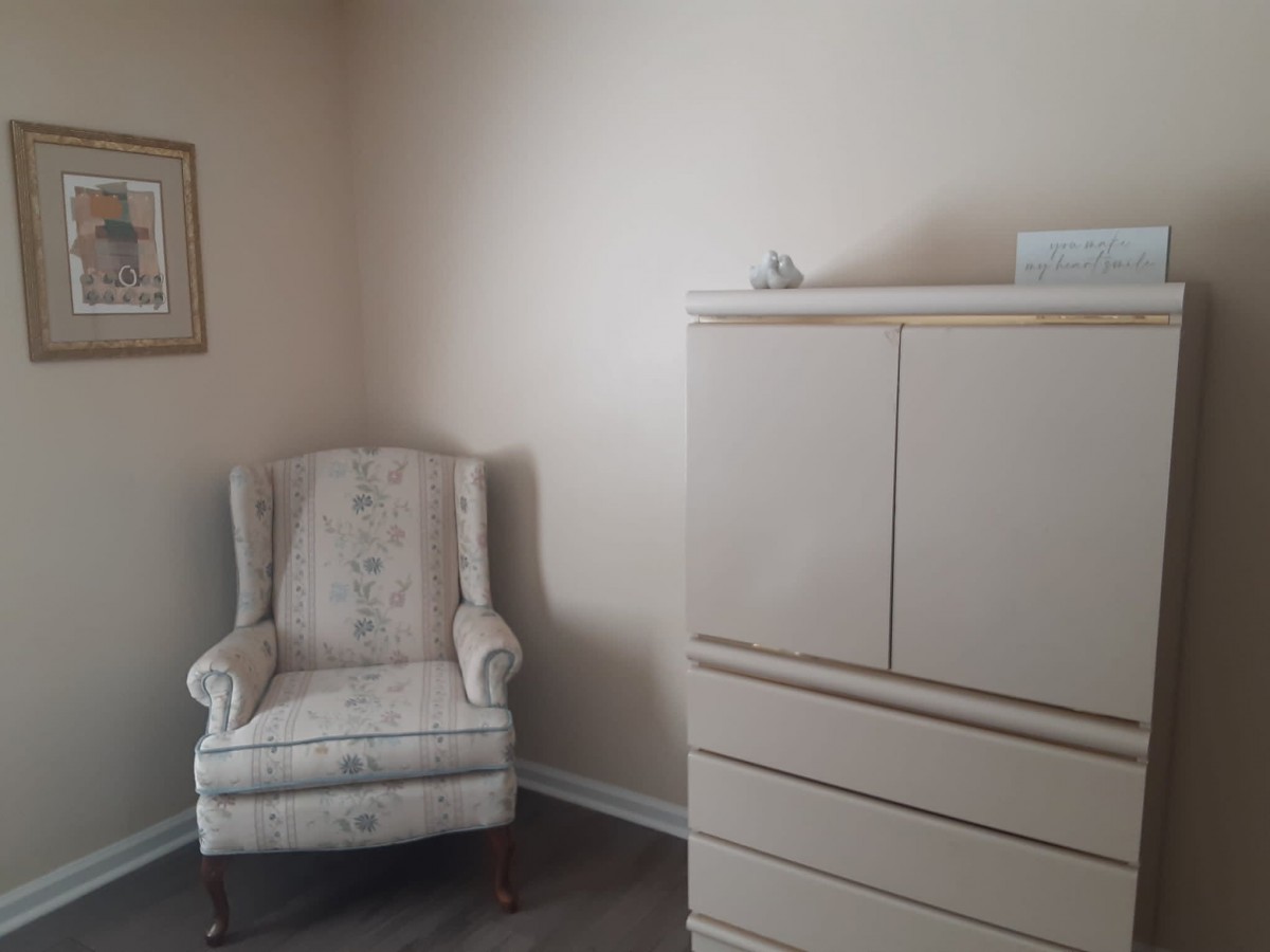 A minimalist room with a floral armchair and a tall dresser.