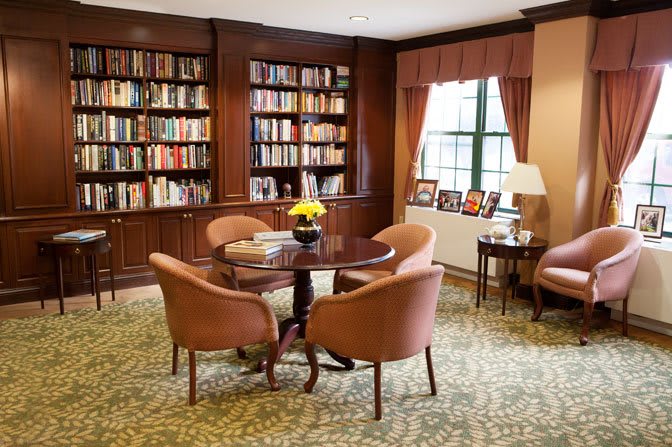 A cozy library with a round table and chairs surrounded by bookshelves.