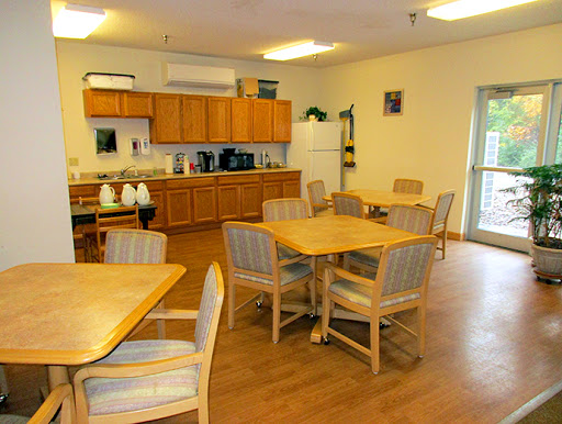 A cozy dining area featuring wooden tables and chairs, with a kitchen in the background.