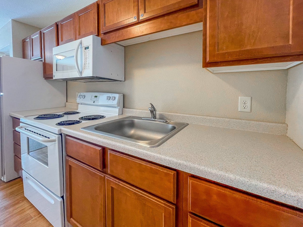 A compact kitchen with wooden cabinets, a stove, microwave, and a sink.